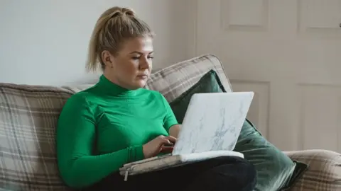 Getty Images Stock image of a woman at home looking at a laptop